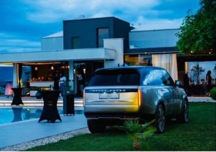 A Range Rover Autobiography parked at dusk in front of Emporia Hotel's illuminated glass-and-stone exterior, beside the pool terrace